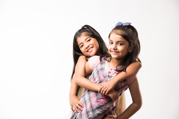 Juguetonas y bonitas hermanas o amigos indios o asiáticos de humor juguetón, abrazándose, bailando, empujándose unos a otros. Aislado sobre fondo blanco