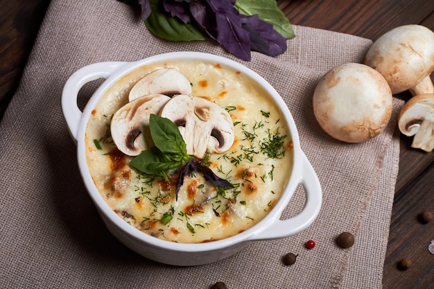 Juliana de pollo con queso, champiñones y hierbas en plato blanco sobre tabla de madera