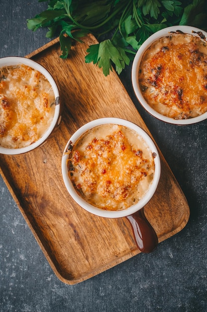 Julienne em porções, cogumelos com creme e queijo, comida de restaurante em um fundo escuro