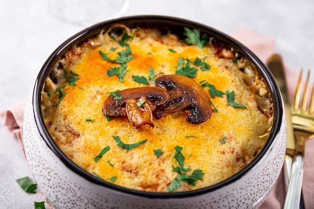 Julienne mit Kartoffeln und Champignons in einer Auflaufform auf hellem Hintergrund