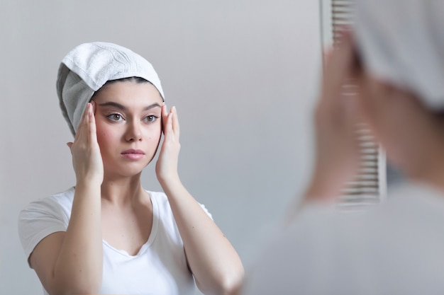 Junge 25-jährige Frau, die sich um ihre Haut im Gesicht kümmert, steht in der Nähe des Spiegels