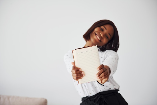 Junge afrikanisch-amerikanische Frau in formeller Kleidung, die drinnen mit Notizblock und leerem Papier in den Händen steht