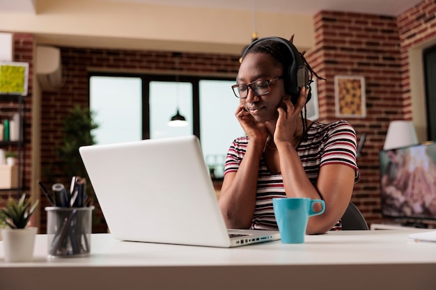 Junge afrikanisch-amerikanische frau mit drahtlosen kopfhörern, die filme online im streaming-dienst auf dem laptop ansieht, freiberuflerin, die eine pause von der arbeit hat. freizeitaktivitäten für teenager, heimunterhaltung