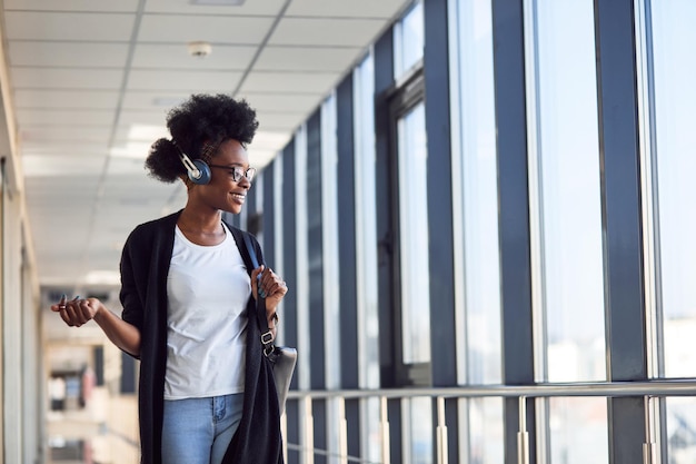 Junge afrikanisch-amerikanische Passagierin in Freizeitkleidung ist am Flughafen und hört Musik über Kopfhörer.