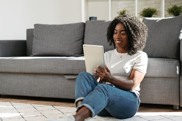 Junge afrikanische Frau, die ein digitales Tablet verwendet und lächelt, während sie sich zu Hause ausruht