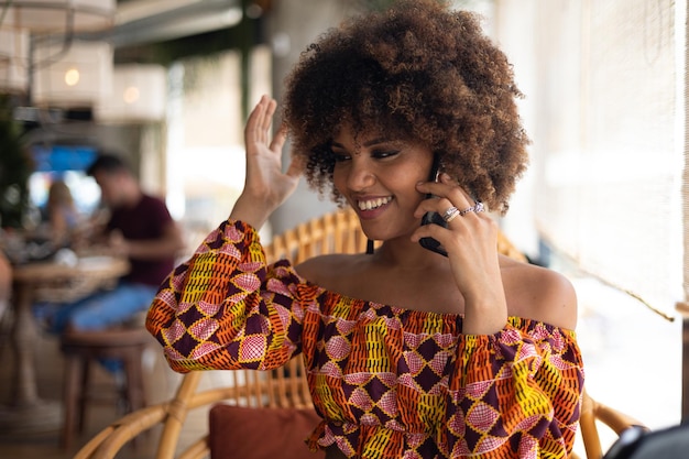 Foto junge afrikanische frau, die in einem restaurant mit dem handy telefoniert