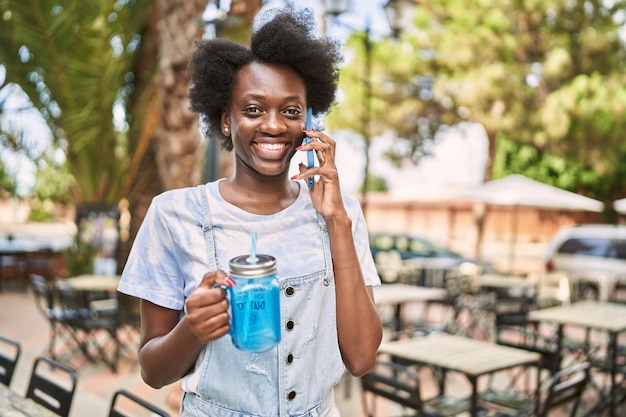 Junge afrikanische Frau, die mit dem Telefon spricht und eine Flasche auf der Straße hält