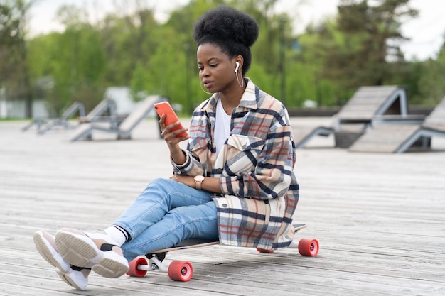 Junge afrikanische Mädchen sitzen auf Longboard mit Smartphone in der Hand Text im Freien im Park mit g-Verbindung