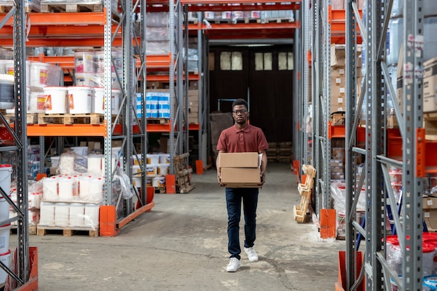 Junge afrikanische männliche Arbeiter des Lagers, die Kisten tragen