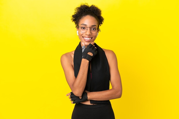 Junge afrikanische Sportfrau isoliert auf gelbem Hintergrund mit Brille und lächelnd