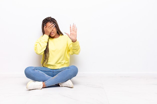 Junge Afro-Frau, die Gesicht mit Hand bedeckt und andere Hand aufstellt