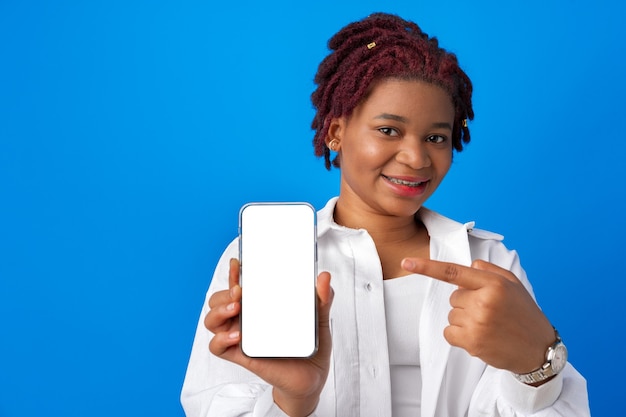 Junge Afro-Frau, die leeren Smartphone-Bildschirm vor blauem Hintergrund zeigt