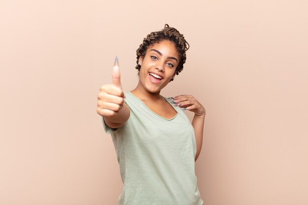 Junge Afro-Frau, die stolz, sorglos, selbstbewusst und glücklich ist und positiv mit Daumen hoch lächelt