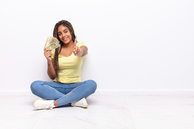 Junge Afro-Frau, die stolz und selbstbewusst lächelt und die Nummer eins triumphierend posiert und sich wie ein Anführer fühlt