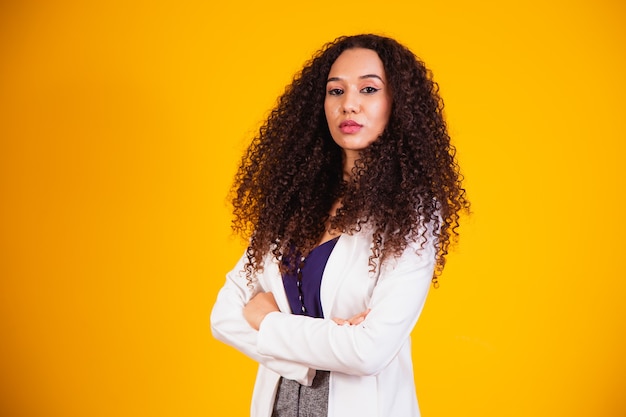 Junge Afro-Geschäftsfrau mit verschränkten Armen auf gelbem Hintergrund.