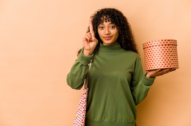 Junge Afroamerikaner-Afro-Frau, die ein Valentinstaggeschenk hält, das Nummer eins mit Finger zeigt.