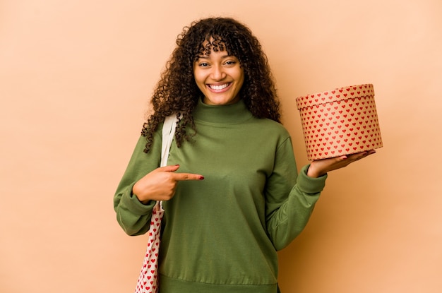 Junge Afroamerikaner-Afro-Frau, die eine Valentinstaggeschenkperson hält, die von Hand auf einen Hemdkopierraum zeigt, stolz und zuversichtlich