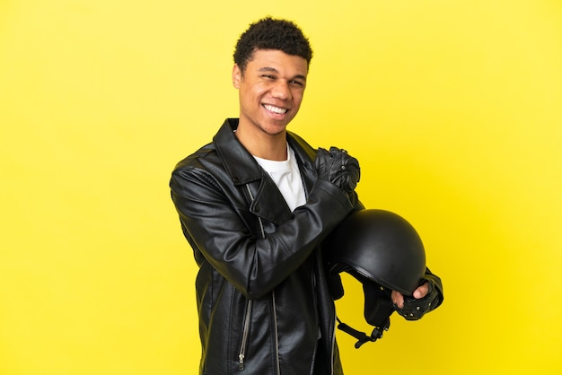 Junge Afroamerikaner mit einem Motorradhelm auf gelbem Hintergrund isoliert einen Sieg feiernd