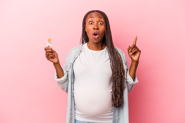 Junge Afroamerikaner schwangere Frau mit Schnuller isoliert auf rosa Hintergrund mit einer großartigen Idee, Konzept der Kreativität.