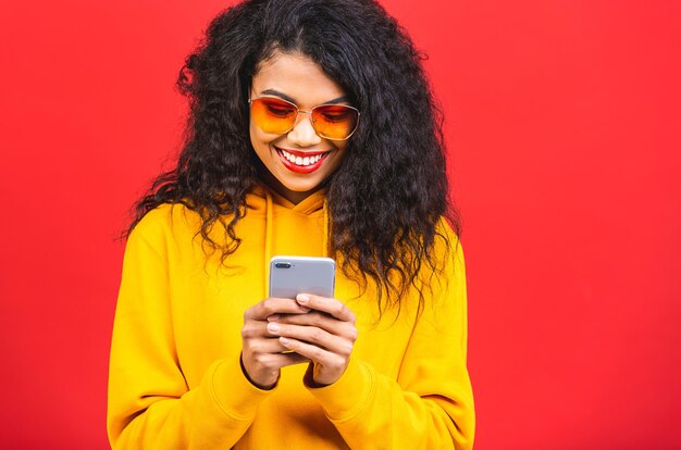 junge Afroamerikaner schwarze Frau mit einem Handy lokalisiert über rotem Hintergrund