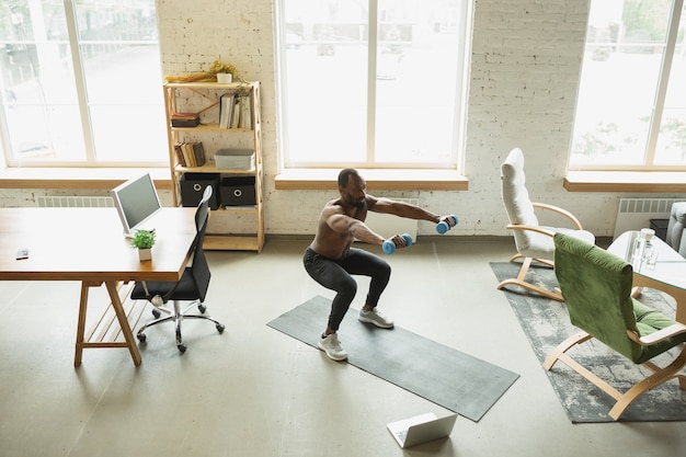 Foto junge afroamerikaner trainieren zu hause während der quarantäne des coronavirus-ausbruchs, machen fitnessübungen, aerobic. sportlich bleiben während der isolierung. wellness, bewegungskonzept. sit-ups.