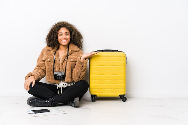 Junge Afroamerikanerfrau bereit für eine Reise, die einen Kopienraum auf einer Handfläche zeigt und eine andere Hand auf Taille hält.