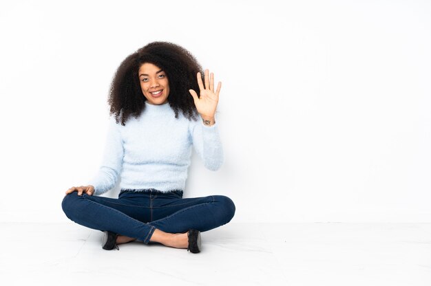 Junge Afroamerikanerfrau, die auf dem Boden sitzt und fünf mit den Fingern zählt