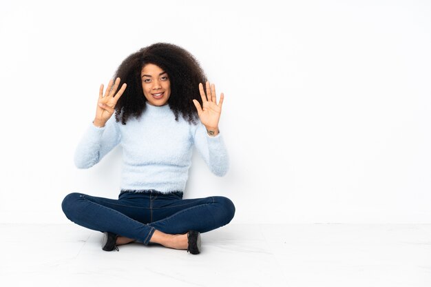 Junge Afroamerikanerfrau, die auf dem Boden sitzt und neun mit den Fingern zählt