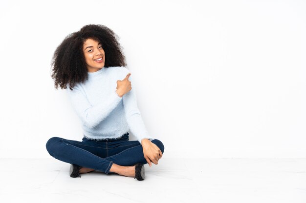 Junge Afroamerikanerfrau, die auf dem Boden sitzt und zurück zeigt