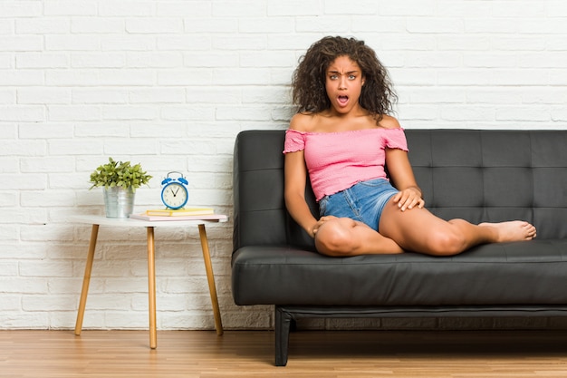 Junge Afroamerikanerfrau, die auf dem Sofa schreit sehr verärgert und aggressiv sitzt