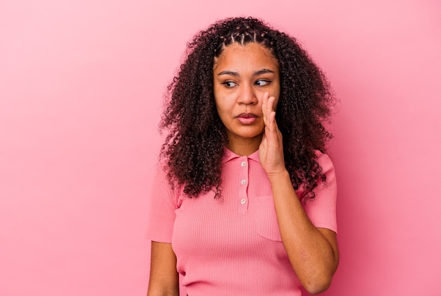Junge Afroamerikanerfrau, die auf rosa Wand isoliert ist, sagt eine geheime heiße Bremsnachricht und schaut zur Seite