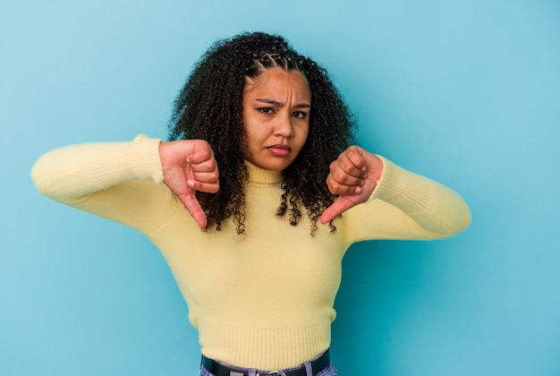 Junge Afroamerikanerfrau, die eine Abneigungsgeste zeigt, Daumen nach unten. Uneinigkeit Konzept.