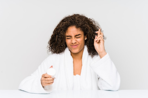 Junge Afroamerikanerfrau, die eine Feuchtigkeitscreme hält, die Finger für Glück hat