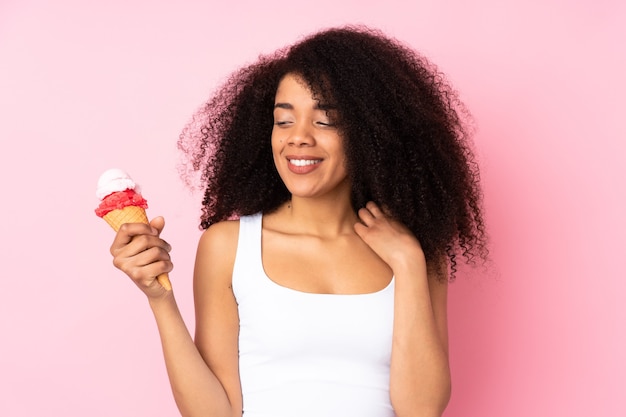 Junge Afroamerikanerfrau, die eine Kornett-Eiscreme lokalisiert auf Rosa hält