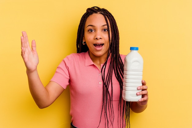 Junge Afroamerikanerfrau, die eine Milchflasche hält, die eine angenehme Überraschung empfängt, aufgeregt und Hände erhebt.