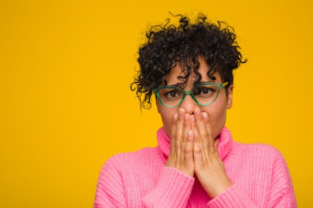 Junge Afroamerikanerfrau, die eine rosa Strickjacke erschrocken und ängstlich trägt.