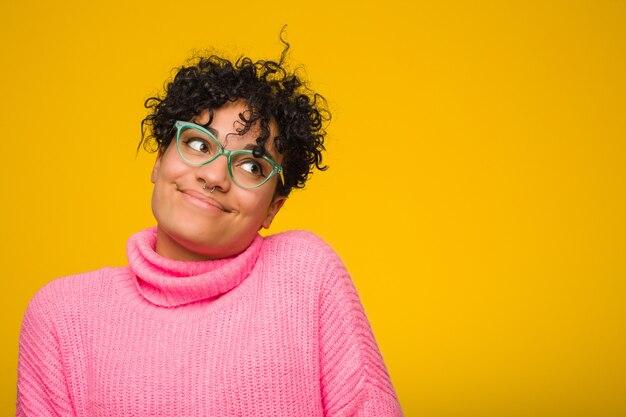 Junge Afroamerikanerfrau, die eine rosa Strickjacke träumt vom Erreichen von Zielen und von Zwecken trägt