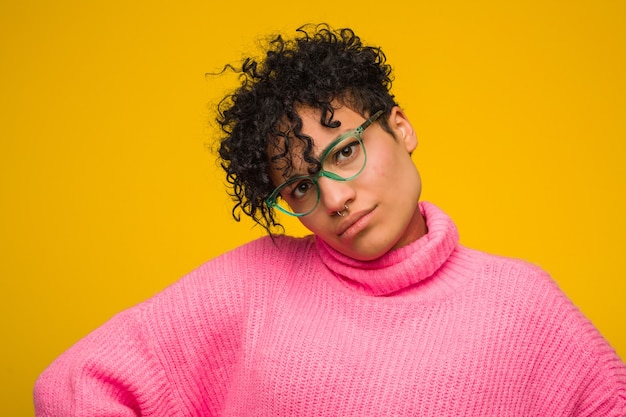 Junge Afroamerikanerfrau, die einen rosa Pullover trägt, der Arme, entspannte Position streckt.