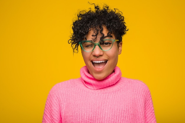 Junge Afroamerikanerfrau, die einen rosa Pullover trägt, der zum Himmel schreit und aufschaut, frustriert.