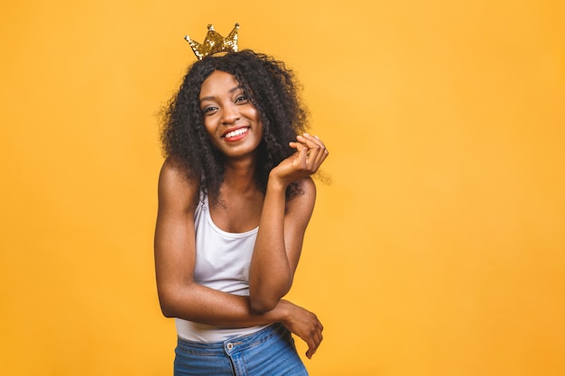 Junge Afroamerikanerfrau, die goldene Krone der Königin mit einem glücklichen und kühlen Lächeln auf Gesicht trägt