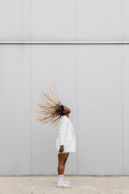 Junge Afroamerikanerfrau, die langes blondes geflochtenes Haar zurück wirft. Platz kopieren. Vertikales Bild