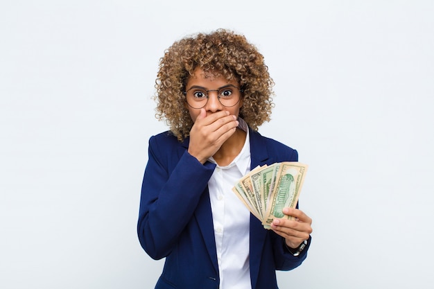 Junge Afroamerikanerfrau, die Mund mit den Händen mit einem schockierten, überraschten Ausdruck bedeckt, ein Geheimnis hält oder Hoppla mit Euro-Banknoten sagt