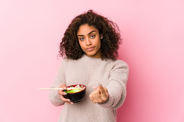 Foto junge afroamerikanerfrau, die nudeln isst, die mit dem finger auf sie zeigen, als ob die einladung näher kommt.