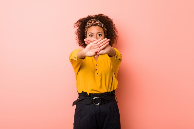 Junge Afroamerikanerfrau gegen eine rosa Wand, die eine Ablehnungsgeste tut