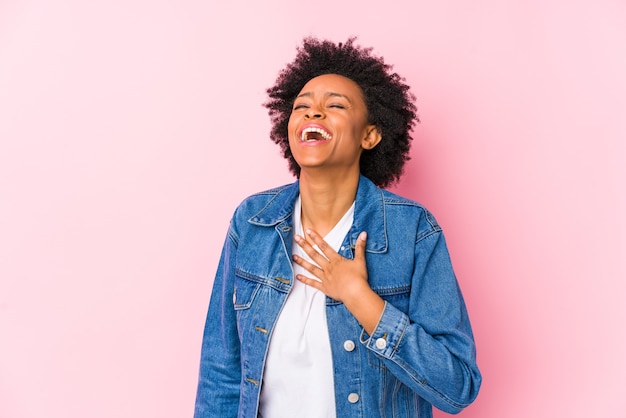 Junge Afroamerikanerfrau gegen einen rosa Hintergrund isoliert lacht laut und hält Hand auf Brust.