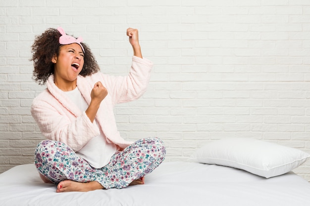 Junge Afroamerikanerfrau im tragenden pijama des Betts, das Faust nach einem Sieg, Siegerkonzept anhebt.