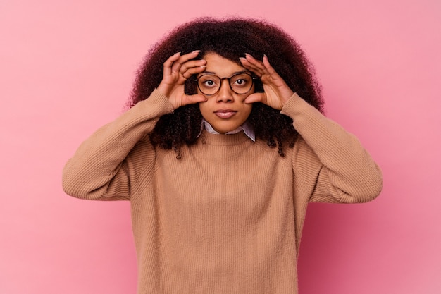 Junge Afroamerikanerfrau isoliert auf rosa Wand, die Augen offen hält, um eine Erfolgschance zu finden.