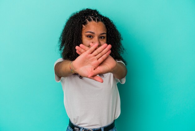 Junge Afroamerikanerfrau lokalisiert auf blauem Hintergrund, der eine Verweigerungsgeste tut