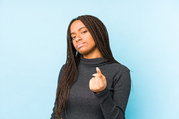 Junge Afroamerikanerfrau lokalisiert auf blauem Hintergrund, der mit dem Finger auf Sie zeigt, als ob die Einladung näher kommt.