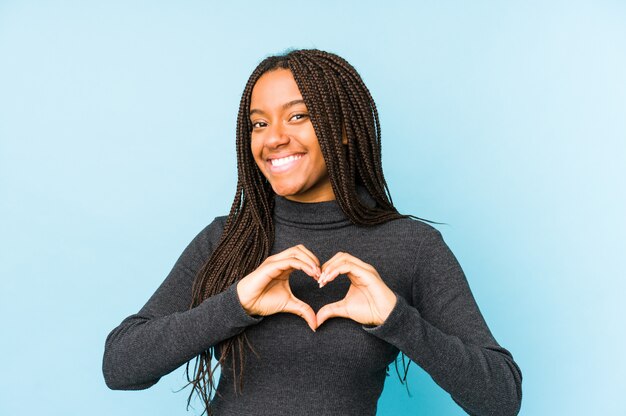 Junge Afroamerikanerfrau lokalisiert auf der blauen Wand, die eine Herzform mit den Händen lächelt und zeigt.